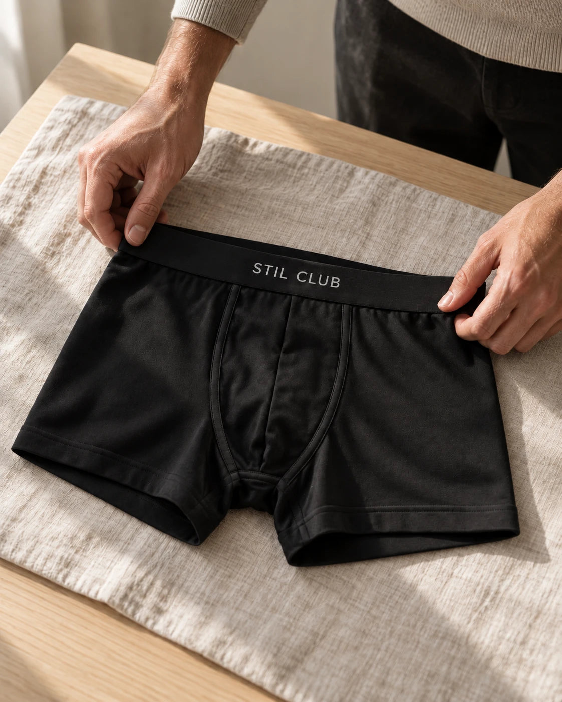 Hands smoothing a pair of black Stil Club boxer briefs on a linen cloth
